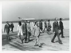 ["Black and white photograph print of Carl Albert walking with several other people at an airport."]