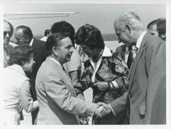 ["Black and white photograph print of Carl Albert and Mary Albert shaking hands with unidentified people at an airport."]