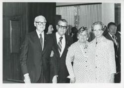 ["Black and white photograph print of an unidentified group of people speaking."]