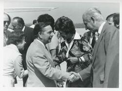 ["Black and white photograph print of Carl Albert and Mary Albert shaking hands with others at an airport."]