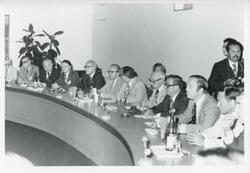 ["Black and white photograph print of Carl Albert, Robert Michel, Melvin Price, Clement Zablocki, John Brademas, and other men seated at a conference table during the House delegation trip. August 1975"]