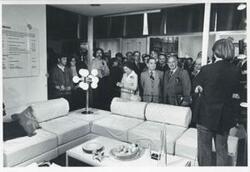 ["Black and white photograph print of Carl Albert and Mary Albert with several other people looking at an exhibit."]