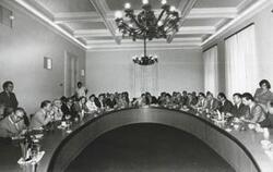 ["Black and white photograph print of several unidentified people seated in a conference room."]