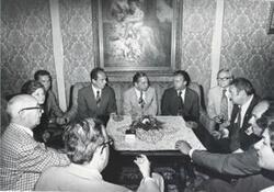 ["Black and white photograph print of Carl Albert seated on a couch with others around him."]