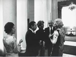 ["Black and white photograph print of Carl Albert and Mary Albert speaking with others."]