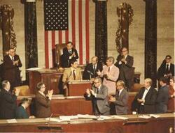 ["Man receiving a standing ovation in House chamber. Carl Albert standing behind speaker. Oversized, color."]