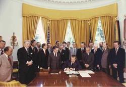 ["Large group of men in Oval Office observing Richard M. Nixon sign a bill. Carl Albert is shown. Color. July 1974 Oversized."]
