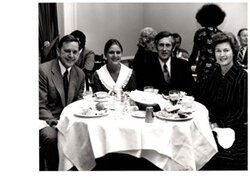["The image depicts Dewey Bartlett seated at a dinner table with Gretchen Moores, Ken Moores, and Ann Bartlett"]