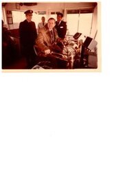 ["The image depicts Dewey Bartlett sits at the helm of the Sergeant Floyd while Colonel Anthony A. Smith and Captain Henry Billiot observe"]