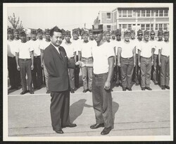 ["Caption: The 1959 Civil Air Patrol National Championship Drill Team from Hawaii look on from the background as the Drill Captain David P. Kalani, III clasps hands with Mr. Dan K. Inouye, the First elected Representative from Hawaii. Stamp: Photograph by B"]