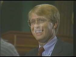 ["In the 1988 campaign ad, Democratic candidate Mitch Irwin showcases his leadership qualities by confidently addressing diverse, attentive crowds at various rallies. Frequently depicted at the podium, Irwin passionately advocates for community-centric policies, engaging with supporters and emphasizing progress. His presence and determined speeches, set against a backdrop of campaign banners, highlight his commitment to impactful governance."]