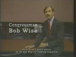 ["In the 1988 political ad for Democratic candidate Robert Ellsworth Wise, a diverse group of elected officials collaboratively discuss state issues and future plans at a large, round conference table. The ad visualizes Wise's commitment to bipartisan cooperation and strategic planning, emphasizing scenes of dialogue and empty chairs symbolizing inclusive leadership potential."]