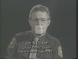 ["In a 1988 campaign ad, Sheriff robustly supports Howard Eliot Wolpe by debunking misleading claims made by Wolpe's opponent. The ad illustrates Wolpe's strong law enforcement record and endorsements through the sheriff's testimonials, filmed with law-related imagery such as American flags and law books, reinforcing Wolpe's reliability and strong stance on law and order."]