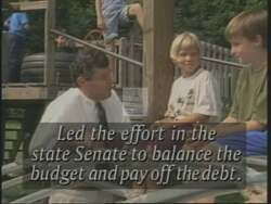 ["In the 1994 political TV ad for John Carroll, the focus is primarily on contrasting his effective fiscal policy and budget-balancing capabilities with those of Congressman Sanders, depicted as a high spender. The ad features scenes of Carroll speaking confidently at rallies, text overlays, and visuals such as graphs showcasing their differing financial management and effectiveness, culminating in a call for responsible leadership."]